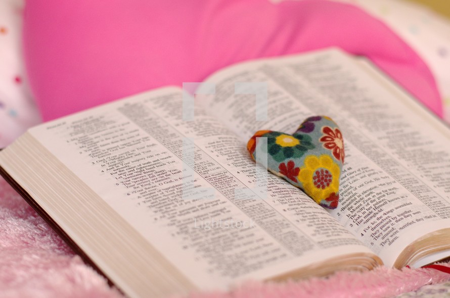 Flowered heart pillow on the pages of an open Bible.