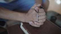 Hands folded in prayer with holding a cross on a Holy Bible in church concept for faith, spirituality and religion, man praying on holy bible in the morning. man hand with Bible praying.