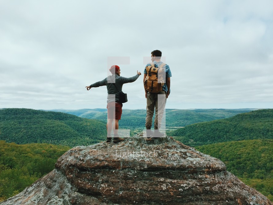 Two hikers standing on a rock pinnacle overlooking forest covered mountains.