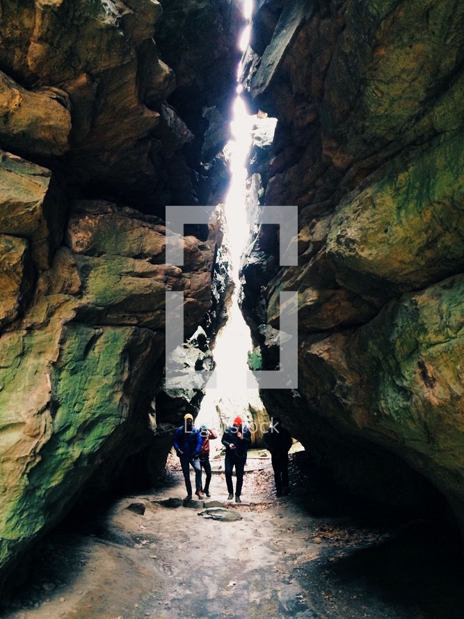 Hikers walking through a cavern between two large boulders.