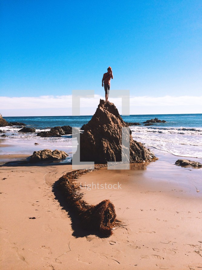 man standing on a rock on a beach 