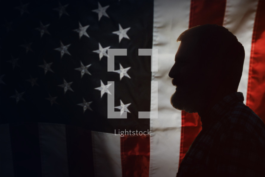 side profile of a bearded man in front of an American flag 