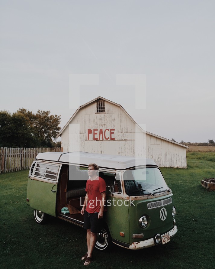 man standing in front of a Volkswagen van and a barn with the word PEACE