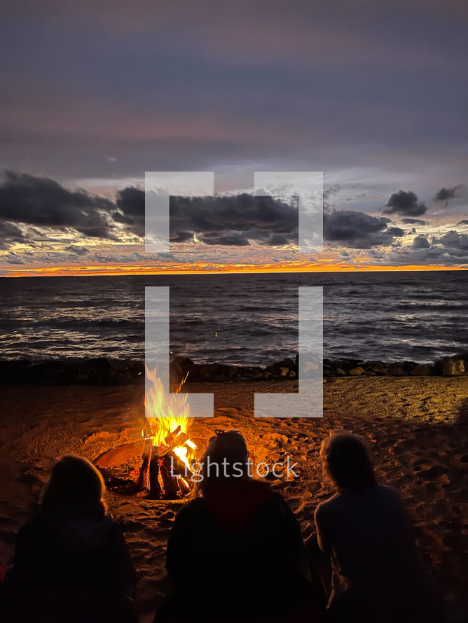 people sitting by a fire on a beach at sunset 