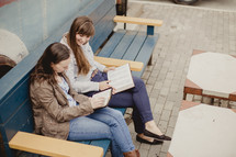 women reading Bibles while sitting on a park bench 