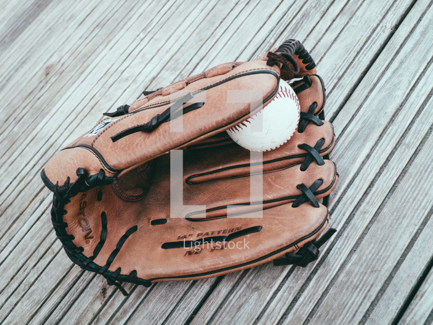A baseball and glove on a wooden tabletop.
