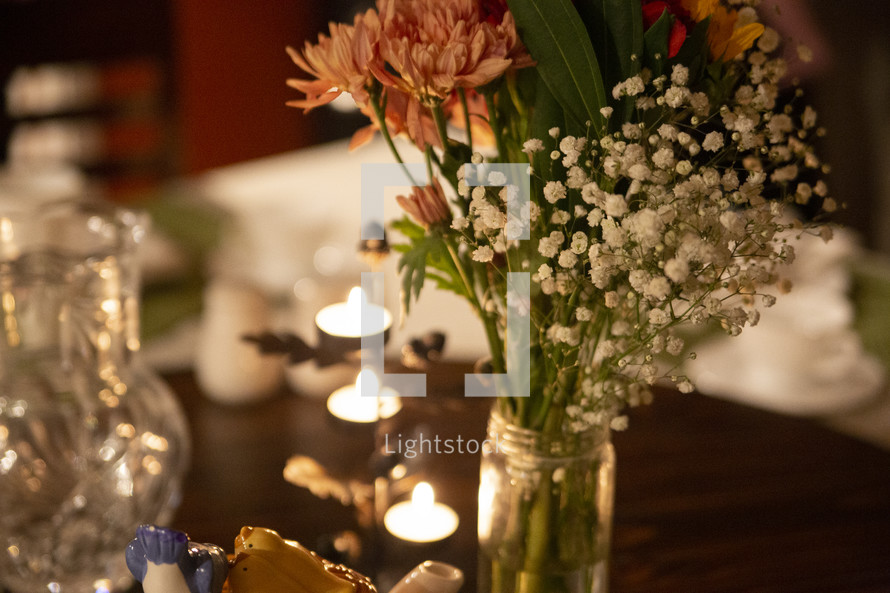 Small bouquet of flowers in a jar on table with candles