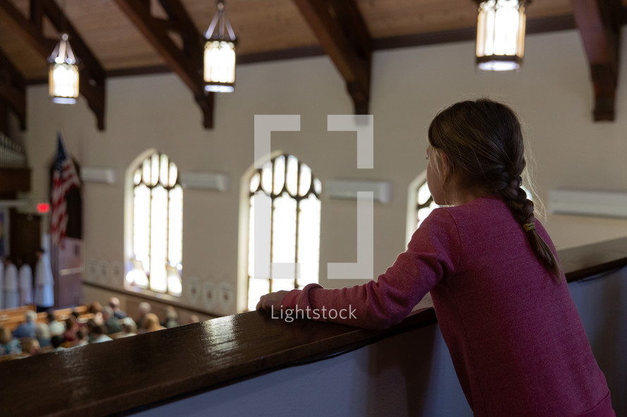 child looking over a railing at the congregation below 