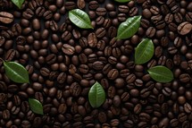 Roasted coffee beans with green leaves on dark background, top view