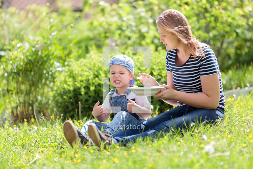 Cute little boy being fed outdoors on the grass