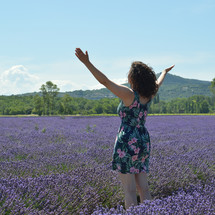 woman standing in a field of lavender with arms raised 