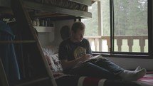 A young male college student reading the Bible in his dorm room.