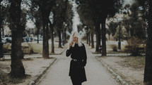 a blonde woman in a black trench coat walking down a sidewalk 