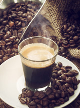 Espresso coffee in glass cup with coffee beans on wooden table