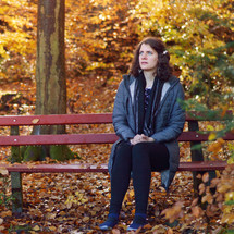 a woman sitting on a bench praying in fall 
