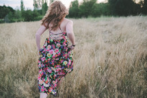 A young woman running through a field of grass in a floral patterned dress.