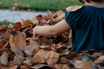 a girl child sitting in fall leaves 