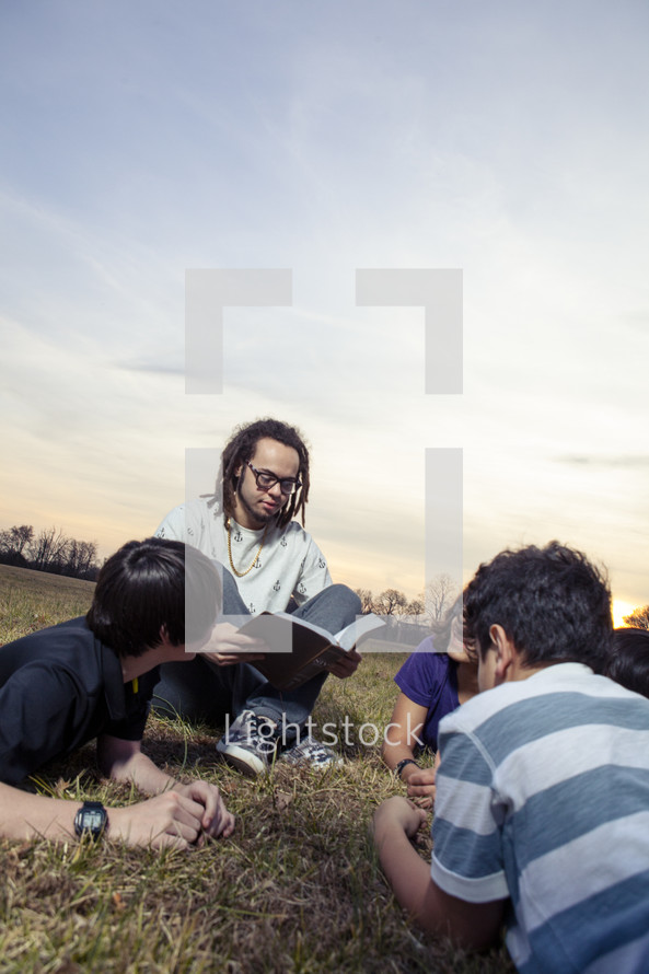 a young man reading a Bible to a group of children 