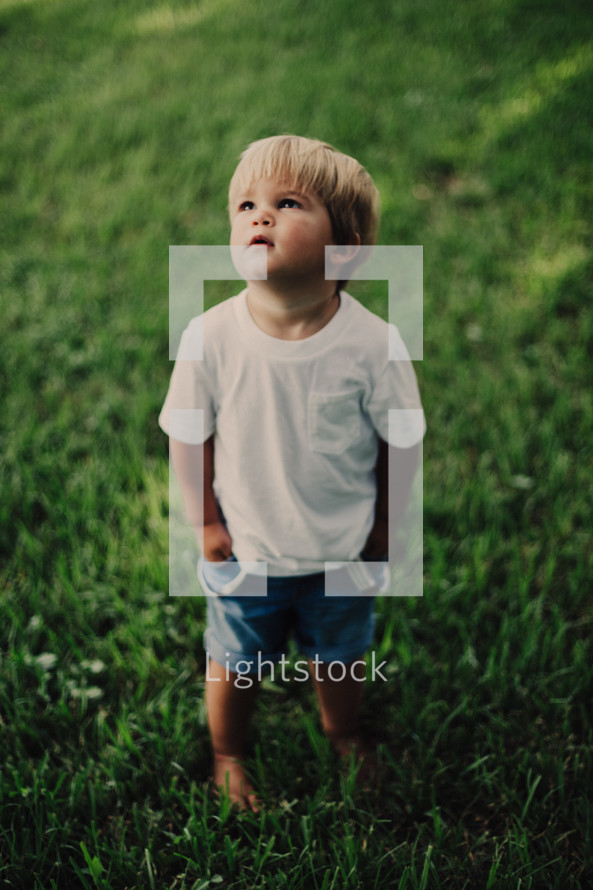 a toddler boy standing in the grass 