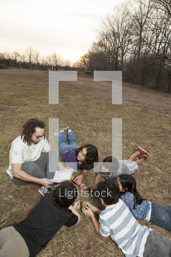 a young man reading a Bible to a group of kids 