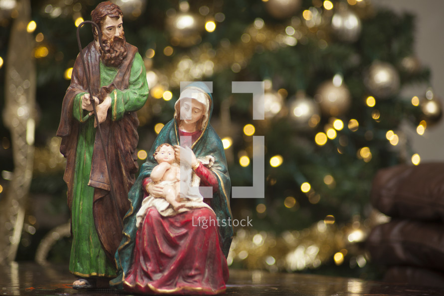 figurines of  Mary, Joseph, and baby Jesus in front of a Christmas tree 