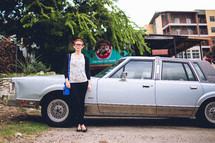 A woman standing in front of an old car. 