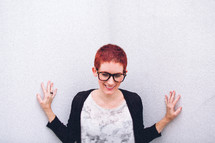 A woman with a pixie haircut touching a white wall. 