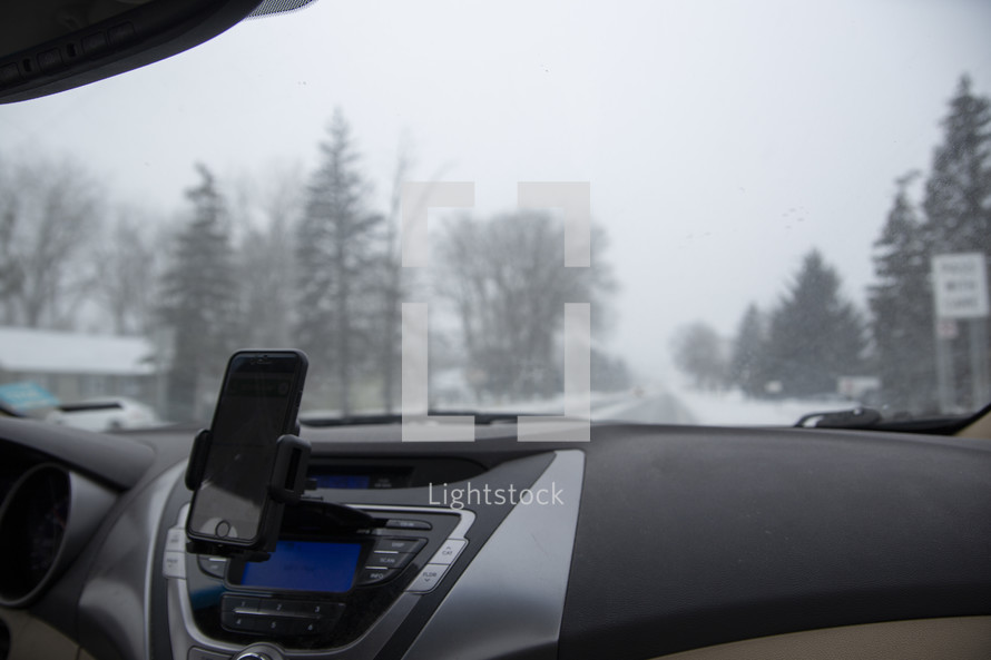 view of a snowy road through a car window and dashboard 