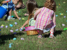 Young Children picking up pastel colored Easter Eggs during a church sponsored Easter Egg Hunt in an open grassy field during Easter. Pastel Colors of light blue, pink, green, fill this image as children wear easter colors and have buckets to pick up Easter Eggs during a church Easter Egg hunt for children. 