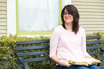 a brunette woman sitting on a bench with a book 