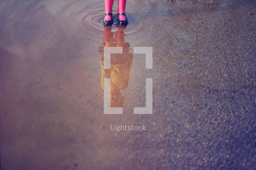 a child splashing in a puddle in rain boots 