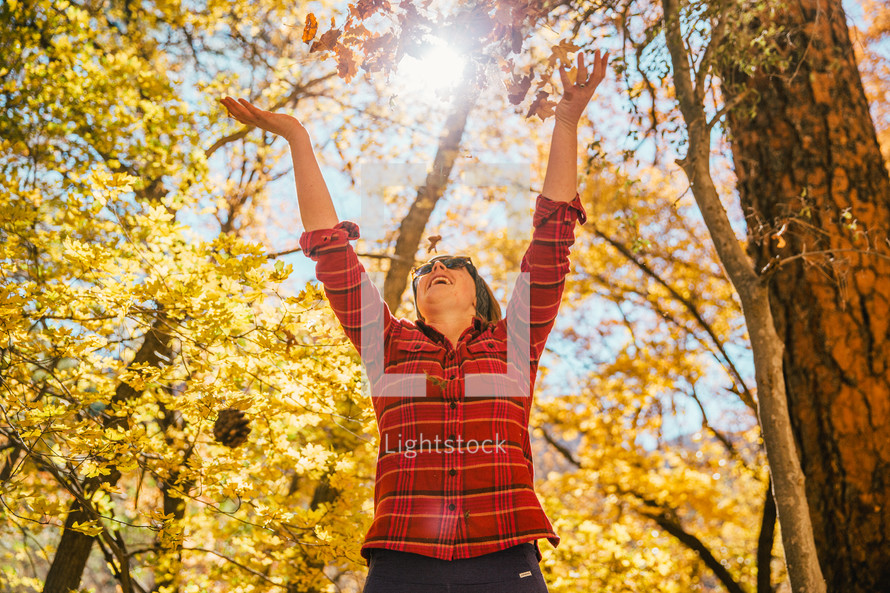 A woman in a forest with arms stretched toward the sky.