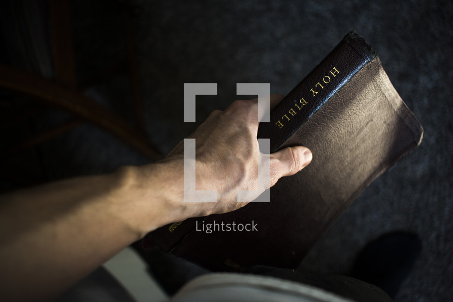 man's arm holding a Bible at his side 