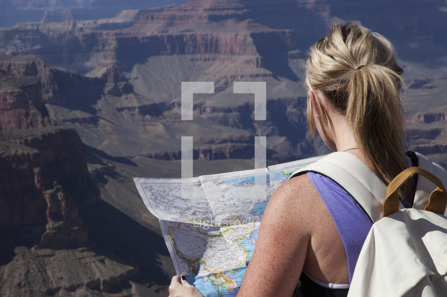 a woman reading a map at the top of a canyon 