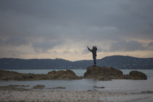 man standing on rocks in shallow water with raised hands 