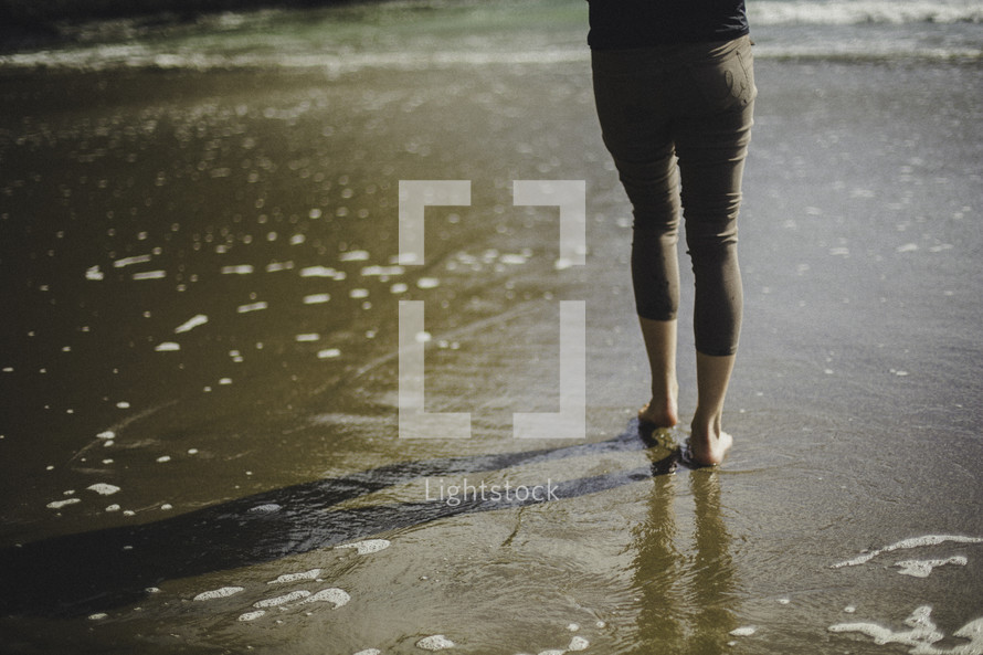 a woman walking barefoot on wet sand 
