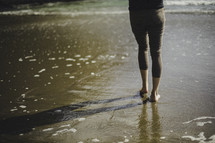 a woman walking barefoot on wet sand 