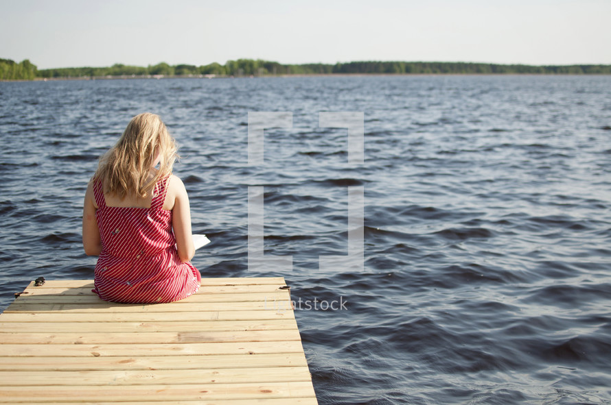 woman reading a Bible sitting on the end of a dock
