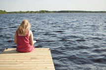 woman reading a Bible sitting on the end of a dock