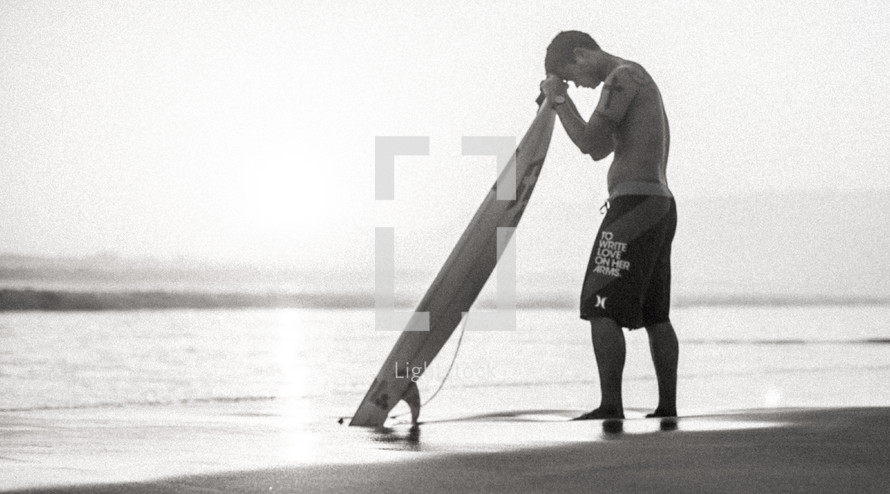 surfer with his head bowed in prayer over his surfboard 