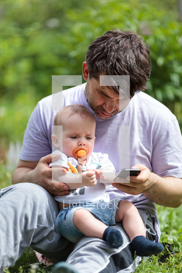 Father using a mobile with baby on his lap
