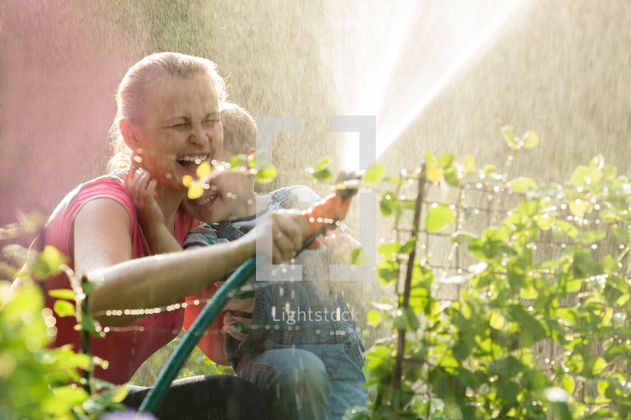Laughing mother and son playing with a sprinkler