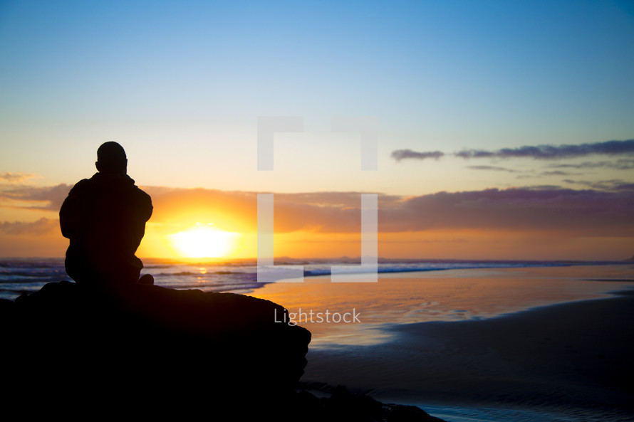 man sitting on a rock on a beach at sunset 