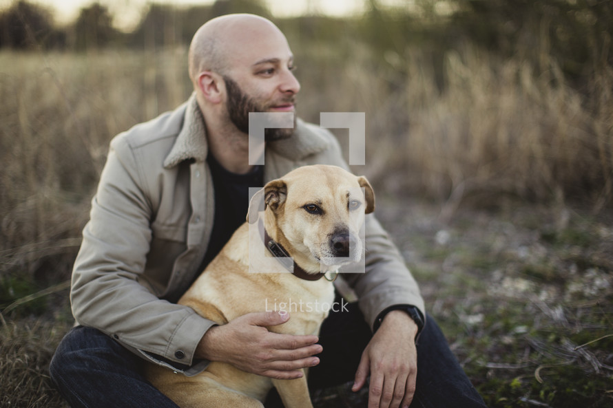 A man with his dog sitting in a field.