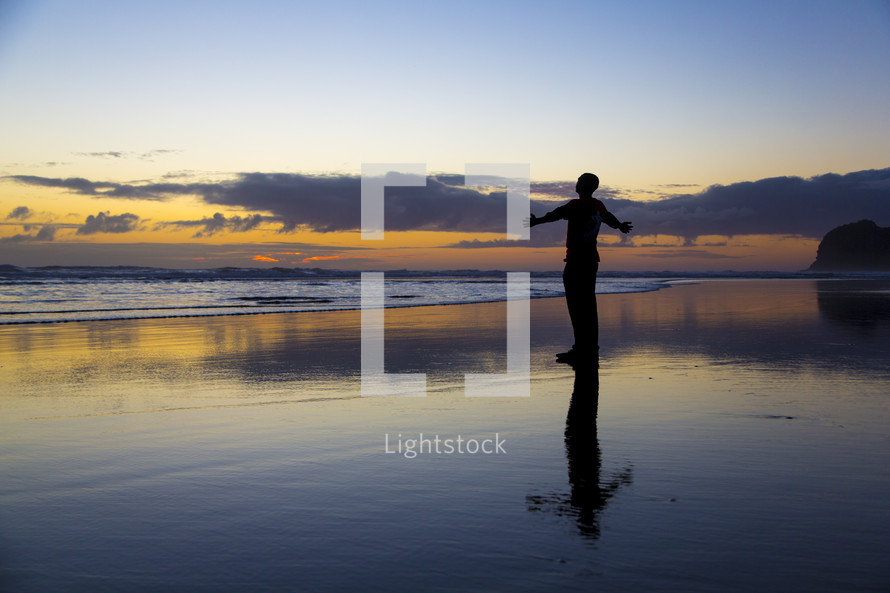 silhouette of a man standing on a beach at sunset with open arms 
