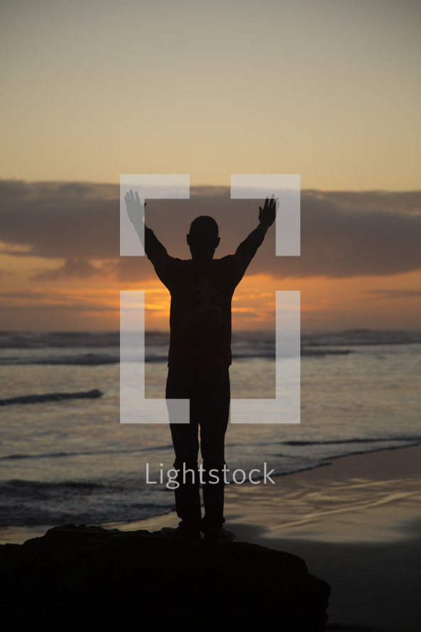 silhouette of a man standing on a beach with hands raised in worship 