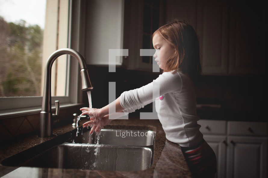 girl child washing her hands at a kitchen sink 