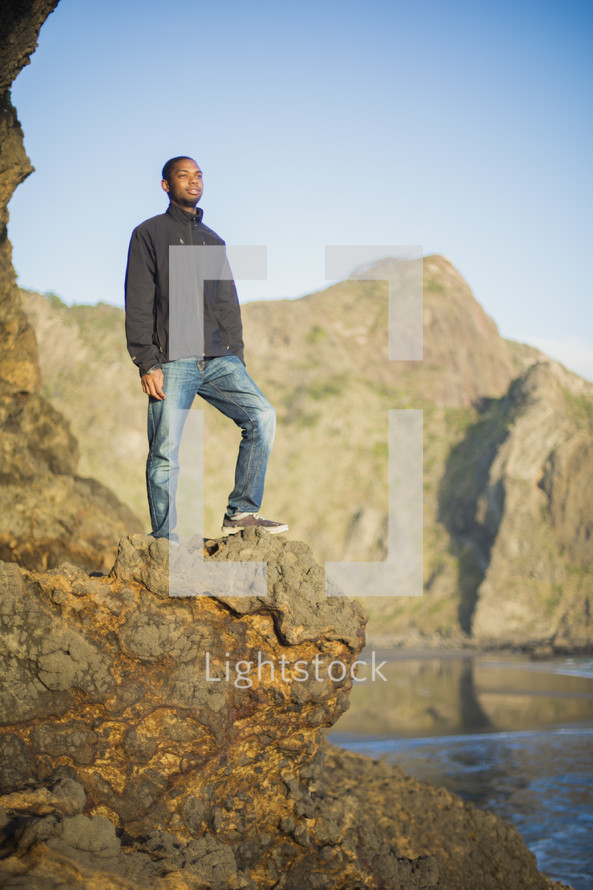 African American man standing on a rock cliff near the ocean 