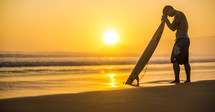 surfer in prayer over his surfboard at sunrise
