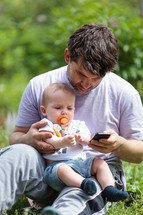 Father using a mobile with baby on his lap